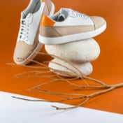 Pair of beige and white leather sneakers balanced on stacked stones, with a dry branch in the foreground.