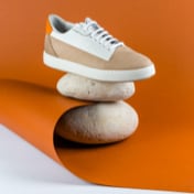 Pair of beige and white leather sneakers balanced on stacked rocks against an orange background.